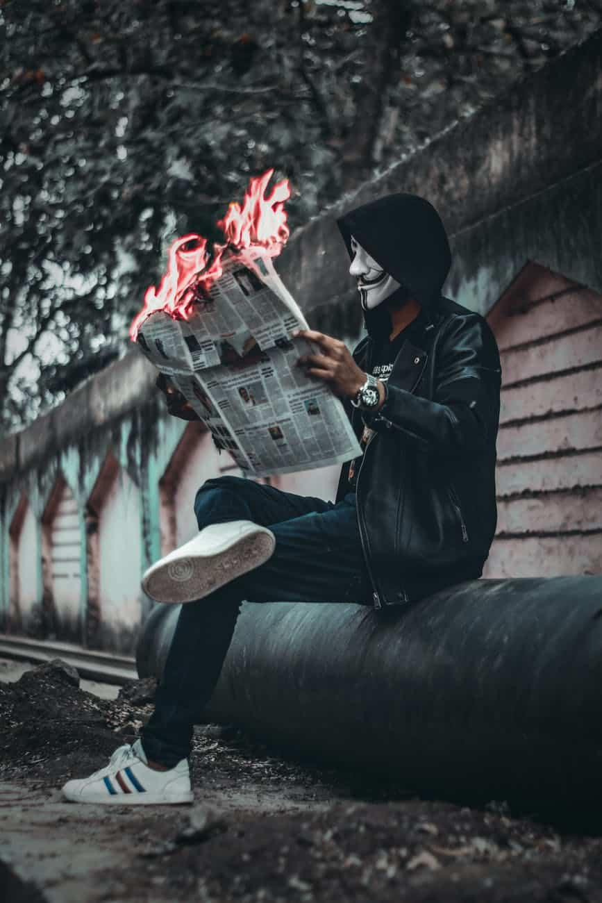 man wearing mask sitting down and holding newspaper with fire
