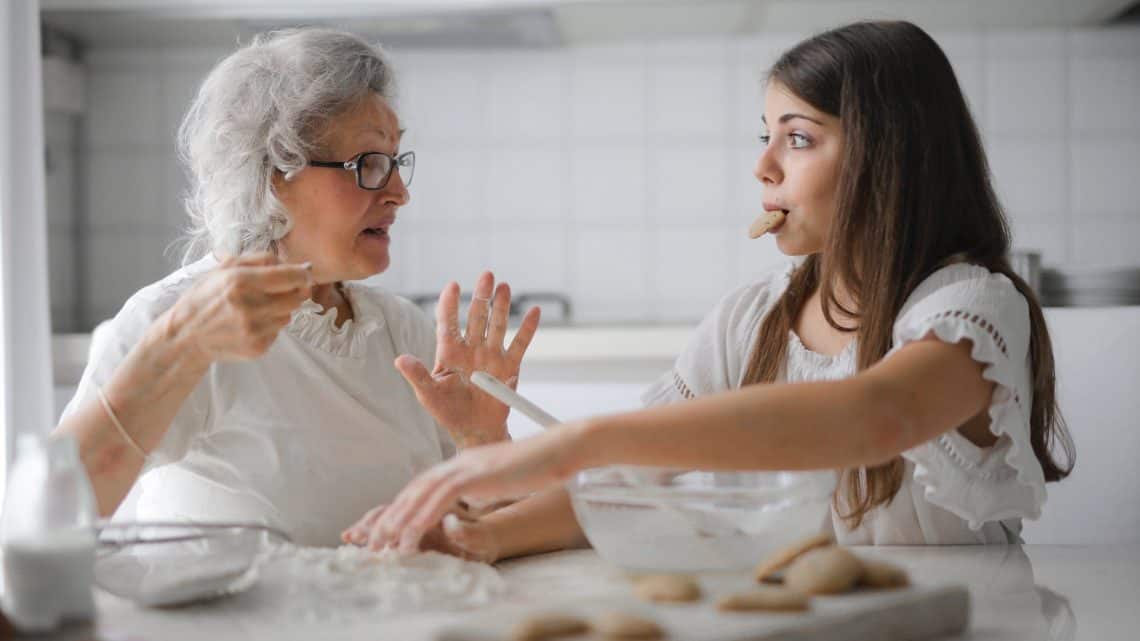 pensive grandmother with granddaughter having interesting conversation while cooking together in light modern kitchen