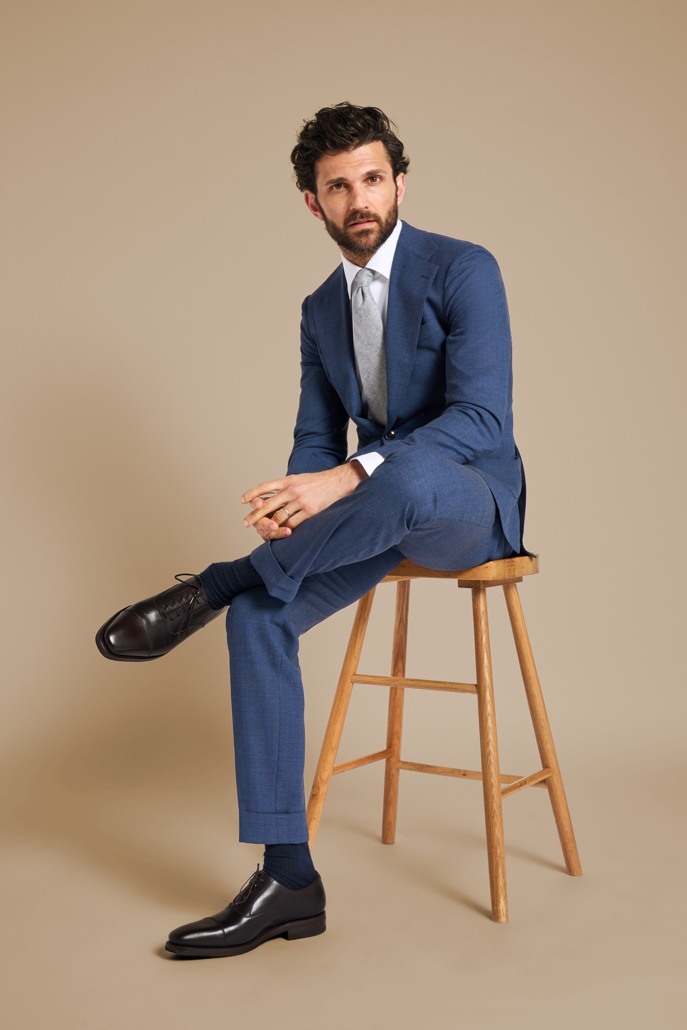 A person in a suit sitting on a stool

Description automatically generated